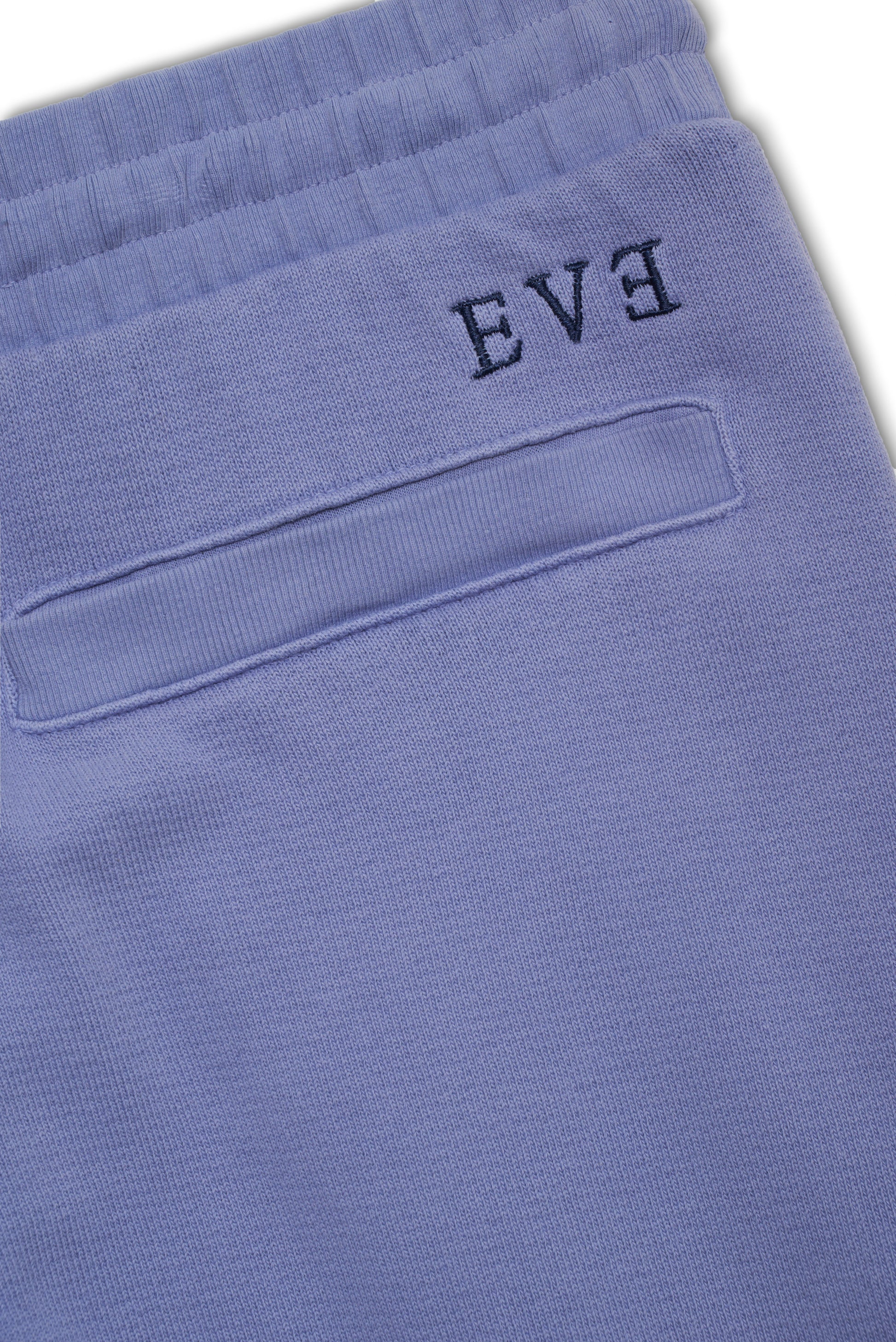 Close-up of blue tapered jogger with ribbed waistband and embroidered text detailing on the pocket.